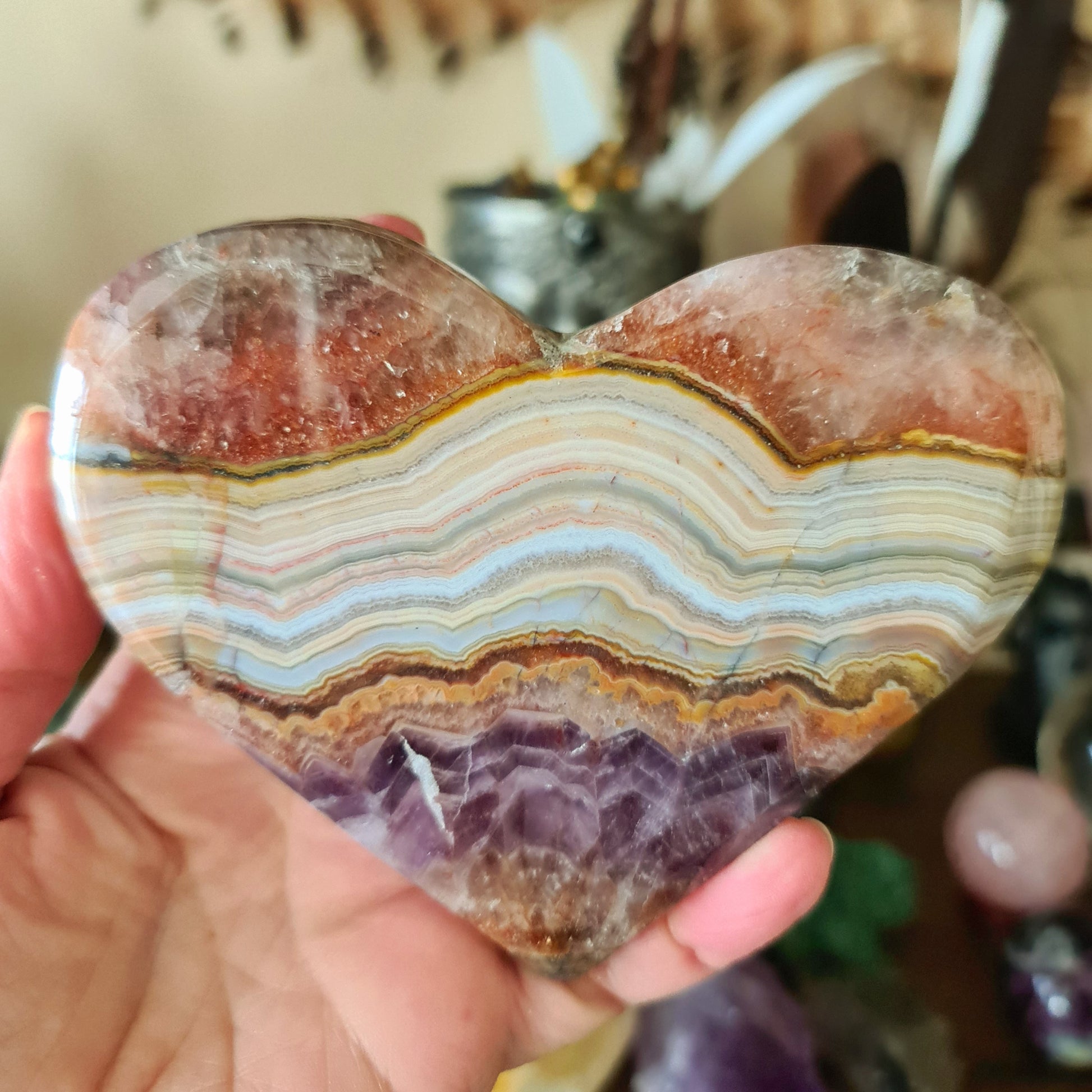 A heart-shaped amethyst agate slab being held in a person's hand.