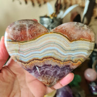 A heart-shaped amethyst agate slab being held in a person's hand.