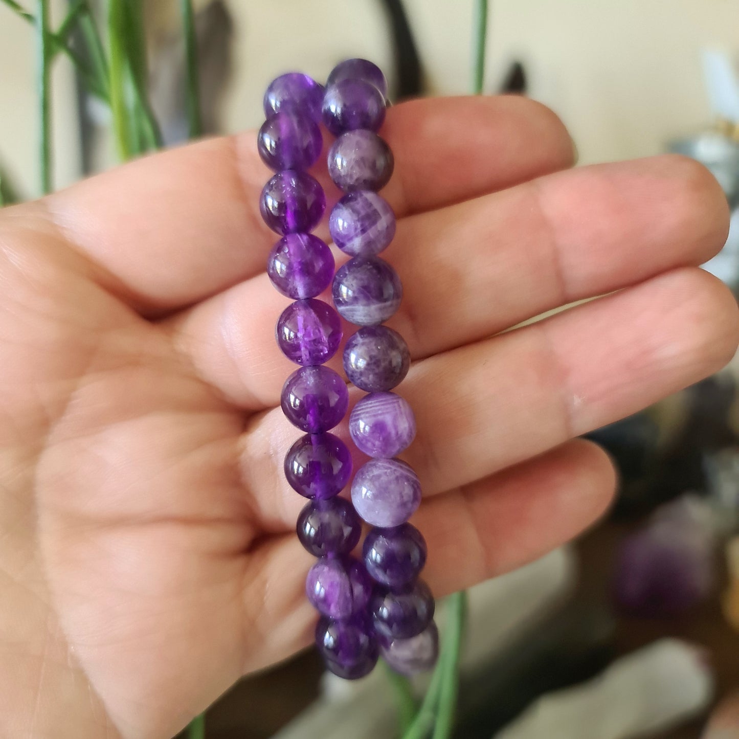 A hand holding a purple amethyst bracelet with a blurred background.