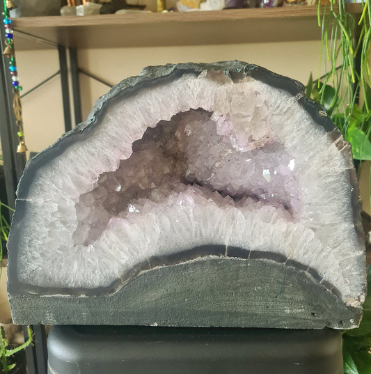 A large amethyst crystal with a cave-like shape, displayed on a platform, with a purple and black color pattern.