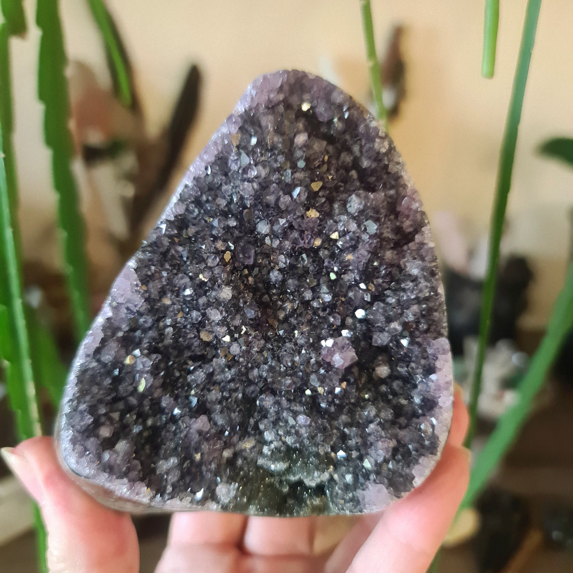 A polished amethyst free-form with natural variations in purple hues and sparkling facets, held in a person's hand.