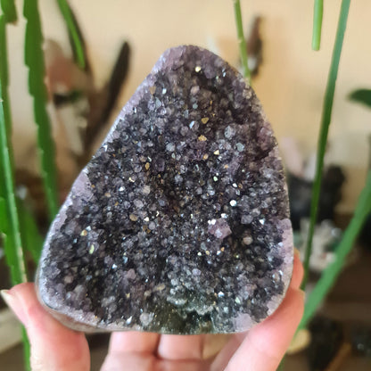 A polished amethyst free-form with natural variations in purple hues and sparkling facets, held in a person's hand.