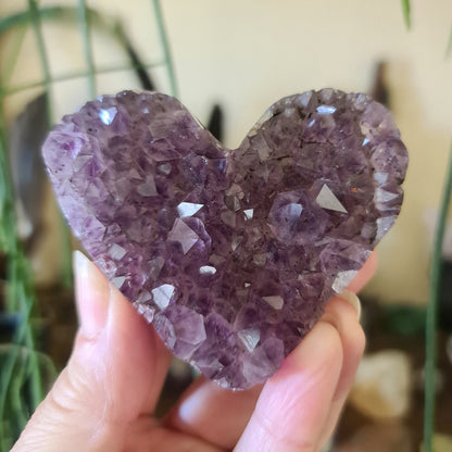 A hand holding a heart-shaped amethyst crystal cluster.