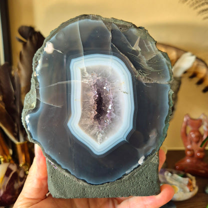 A person holding a polished amethyst geode with a visible purple and white crystal inside.