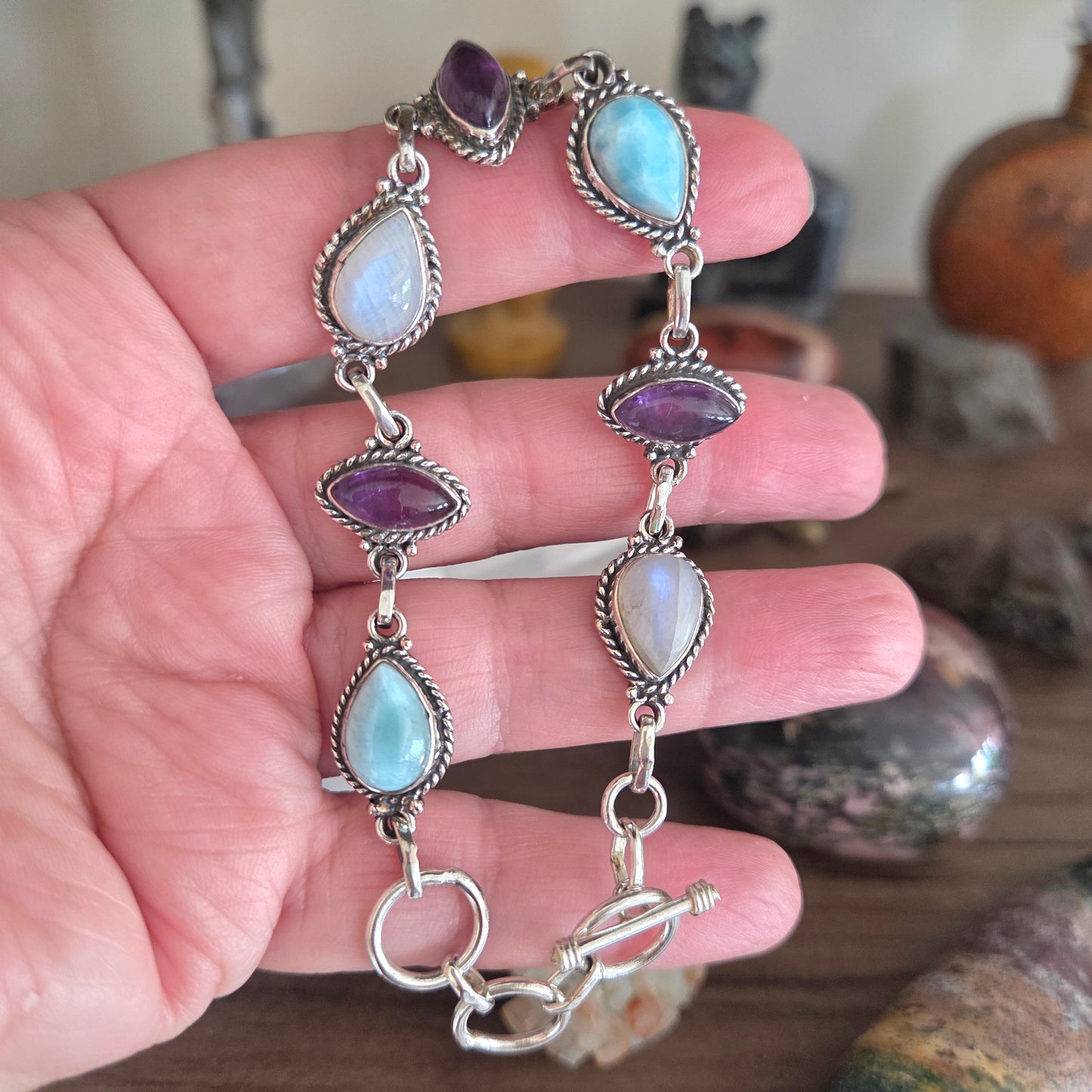 Silver bracelet with gemstones held in a hand against a blurred background