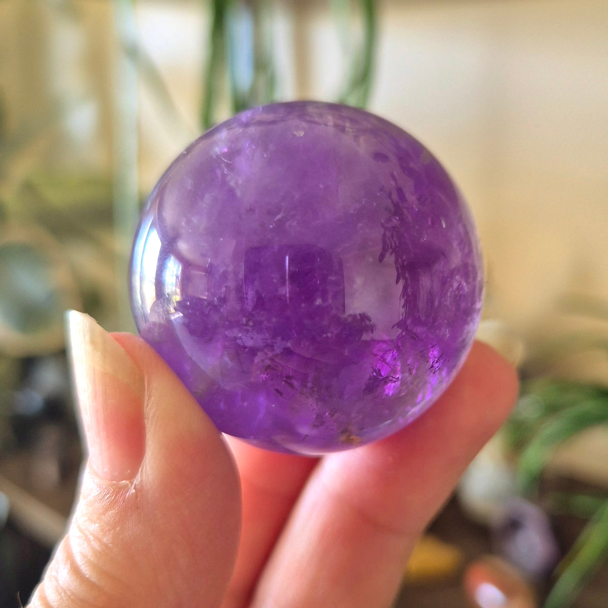 A hand holding a large, polished purple amethyst sphere.