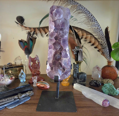 Amethyst crystal on a stand with various crystals and objects on a wooden surface.