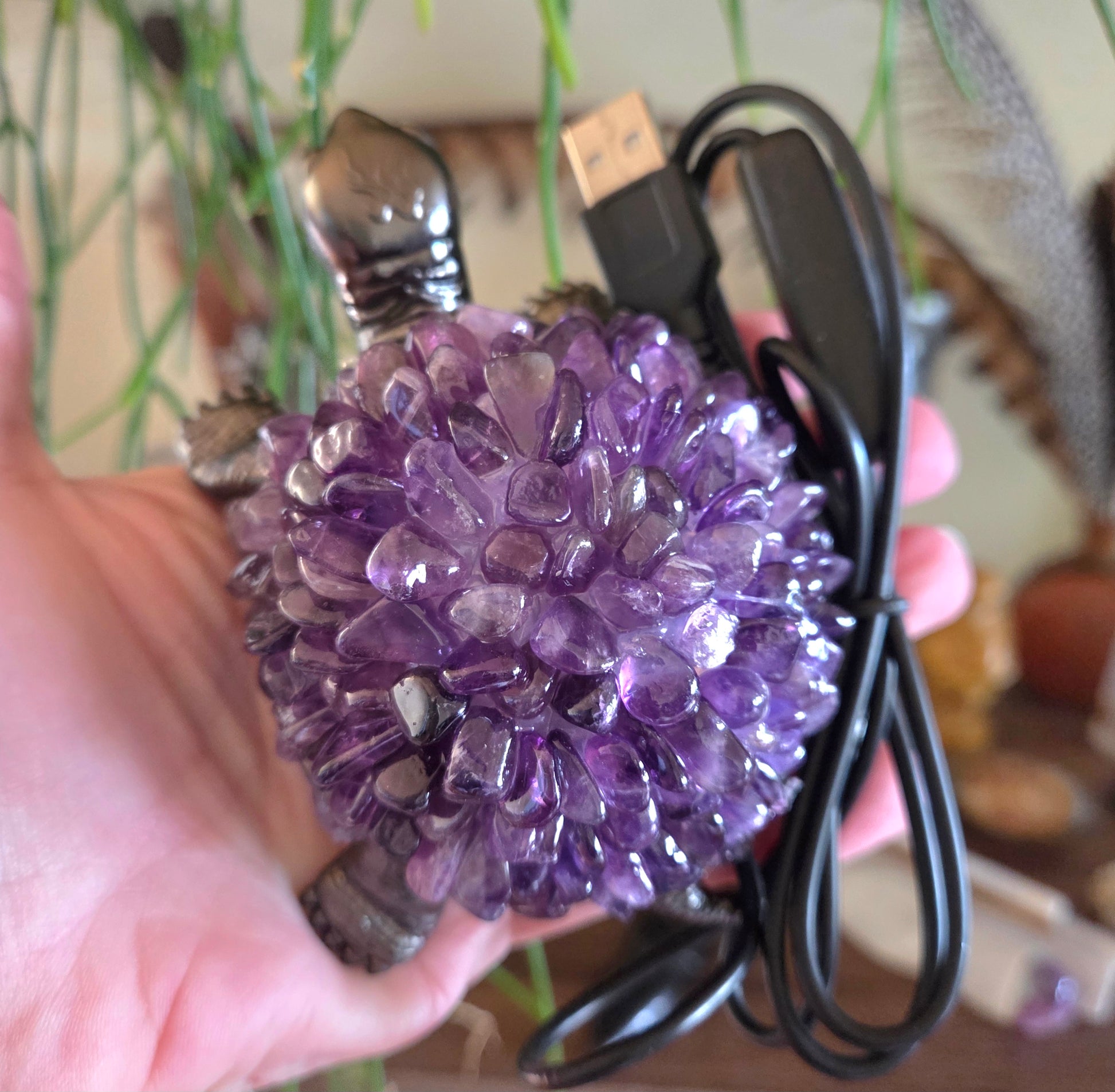 Hand holding a purple crystal ball with a USB cable attached, blurred background