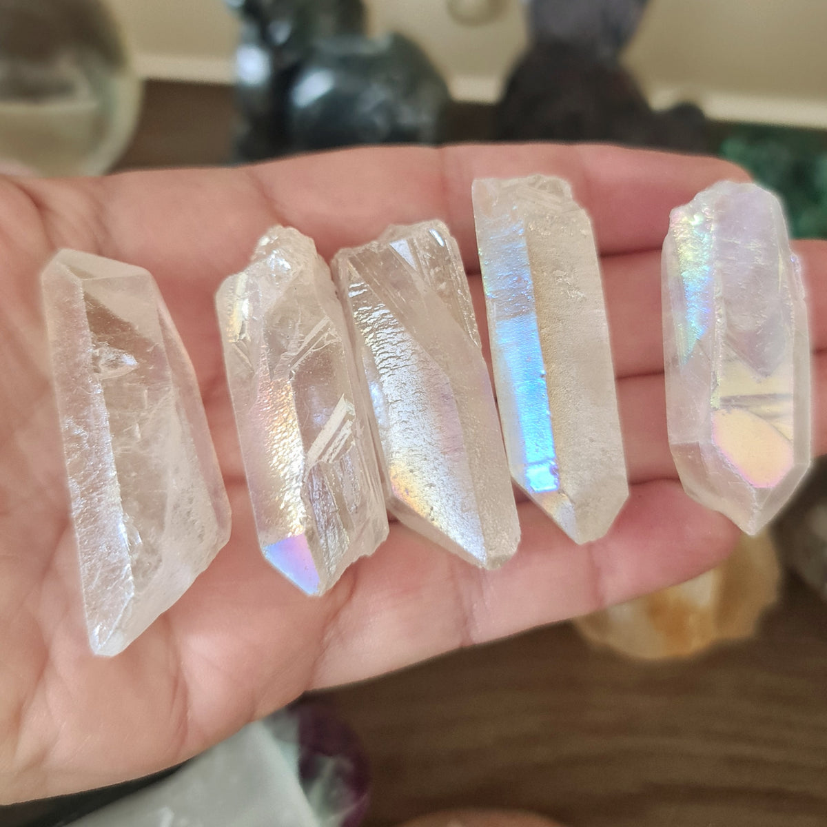 A hand holding several clear crystal points with a rainbow sheen.