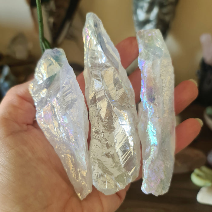 A hand holding three angel aura quartz crystal wands with a reflective, glittery surface.