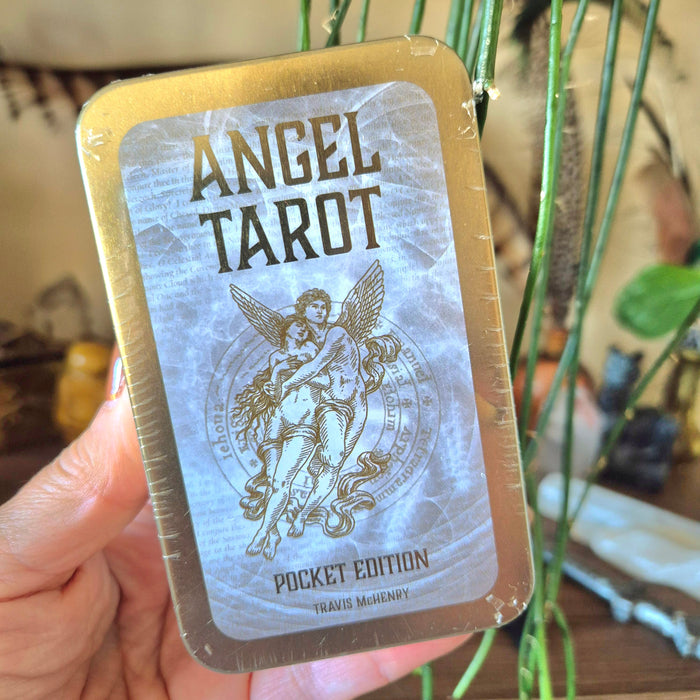 A hand holding a pocket-sized book titled 'ANGEL TAROT' with an illustration of an angel on the cover.
