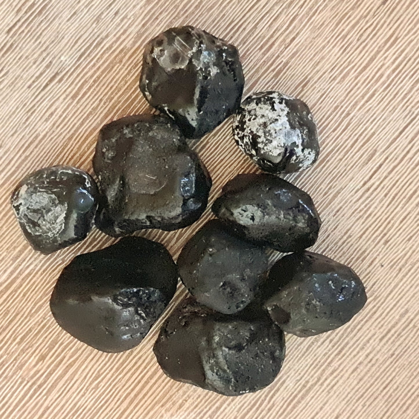 A collection of black stones with white speckles, arranged on a wooden surface.