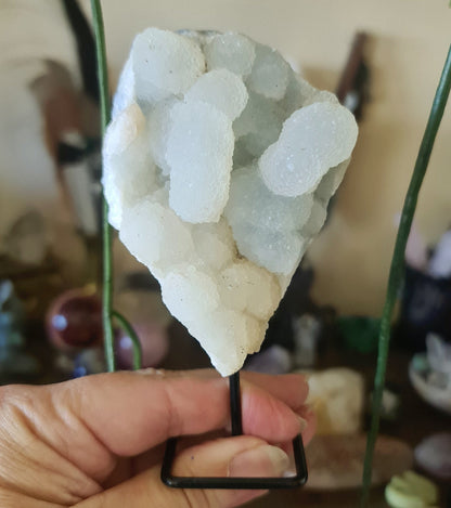 A crystal cluster pin with a metallic appearance, mounted on a black pin, held between fingers.