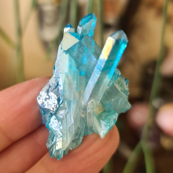 A small blue aura crystal cluster held between fingers, displaying its shiny and translucent properties.