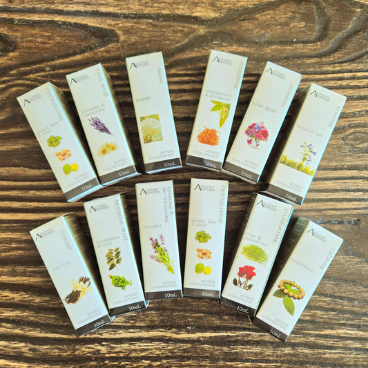 A collection of Aroma Concentrate Oil bottles displayed in a fan-like arrangement on a wooden surface. Each bottle has a label with a different floral or botanical design.