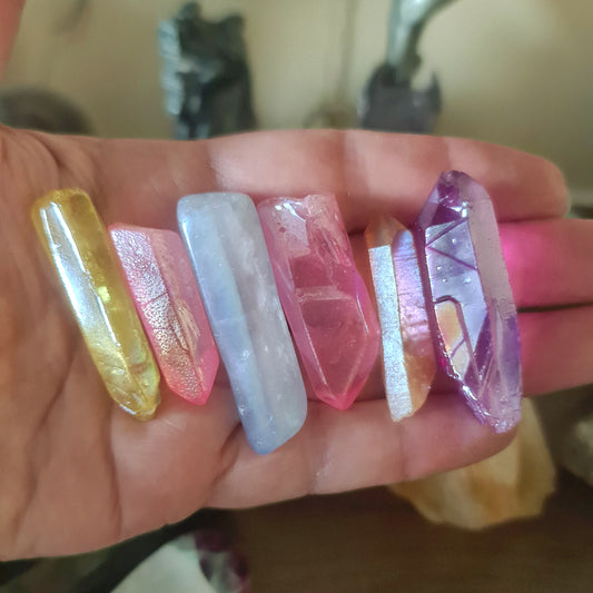 A collection of Aura Quartz crystals in various colors held in a person's hand.