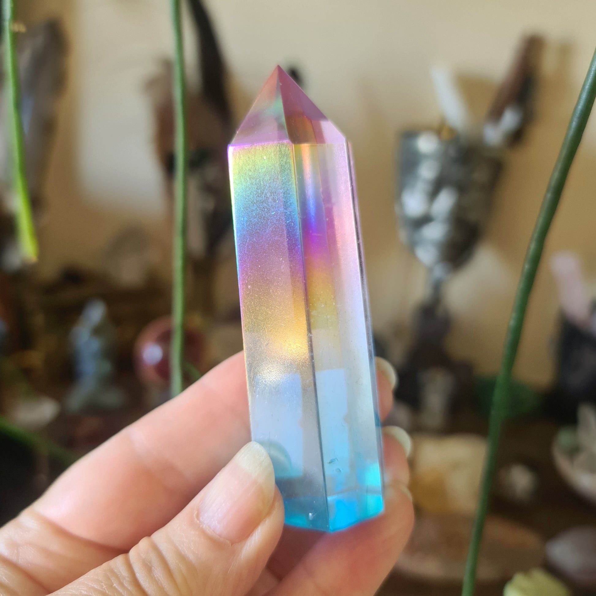 A hand holding a Aura Quartz crystal with a silvery iridescent exterior displaying rainbow-like colors.