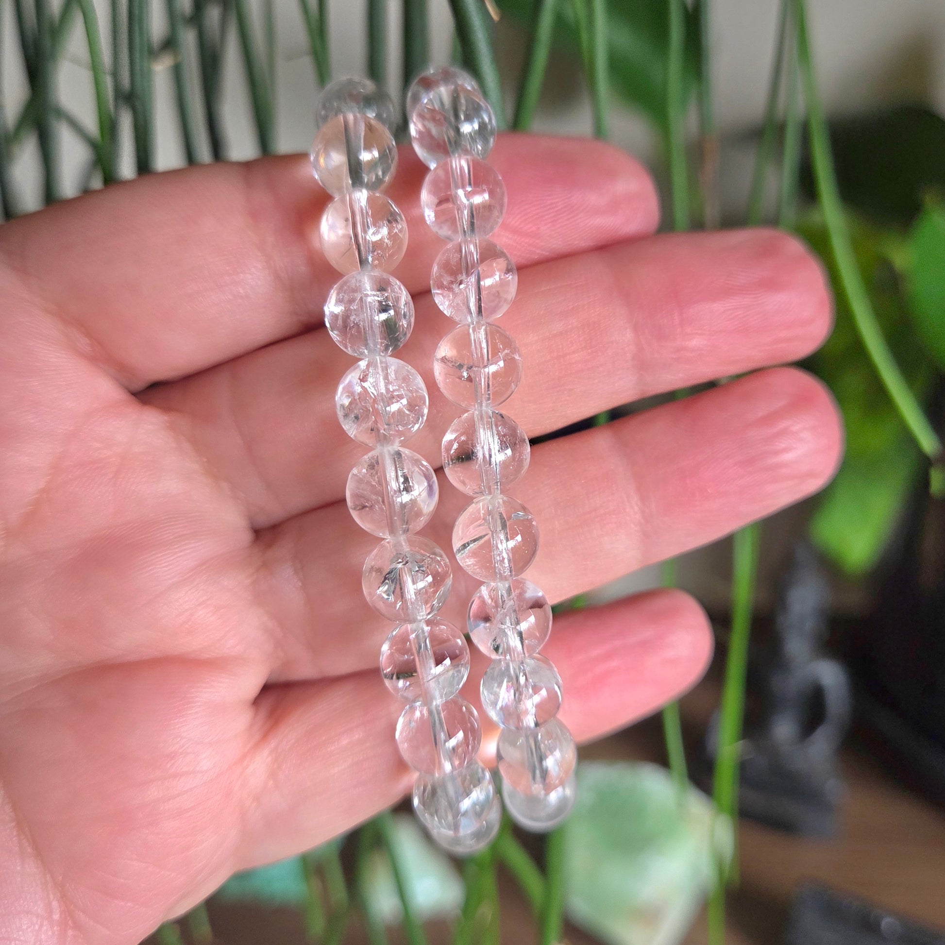 Clear beaded necklace held in a hand with a blurred green plant background