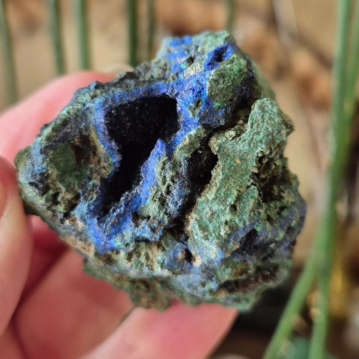 A raw Azurite Malachite mineral specimen held in a person's hand, displaying its natural rugged texture and typical green color with hints of blue.