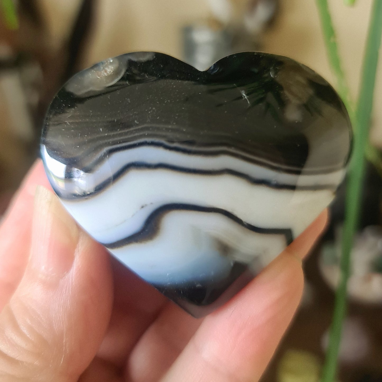 A heart-shaped black agate gemstone with white and gray marbling, held in a person's hand.