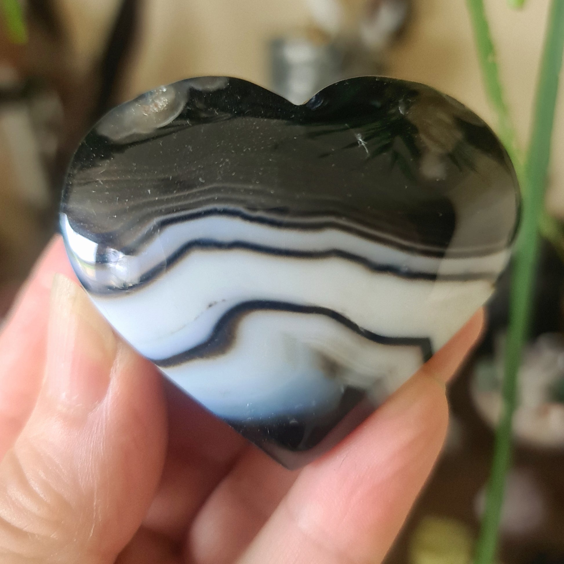 A heart-shaped black agate gemstone with white and gray marbling, held in a person's hand.
