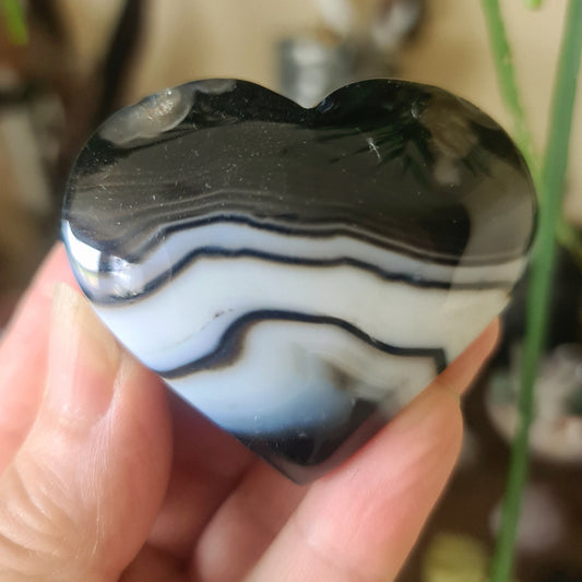 A heart-shaped black agate gemstone with white and gray marbling, held in a person's hand.