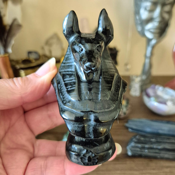 A hand-carved black obsidian stone sculpture of Anubis, held in a person's hand.