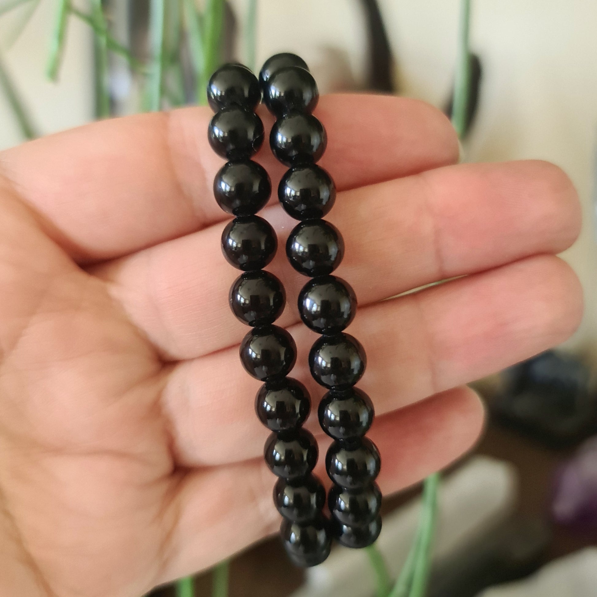 A black obsidian bracelet held in a person's hand, with no visible patterns or designs.