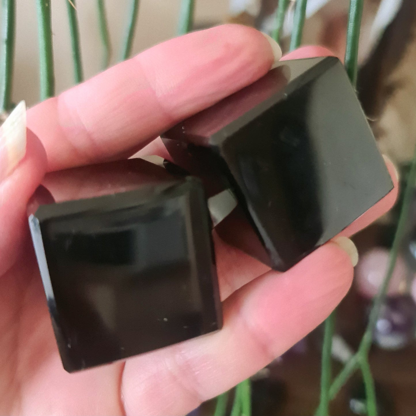 A person holding a small black obsidian cube in their hand.