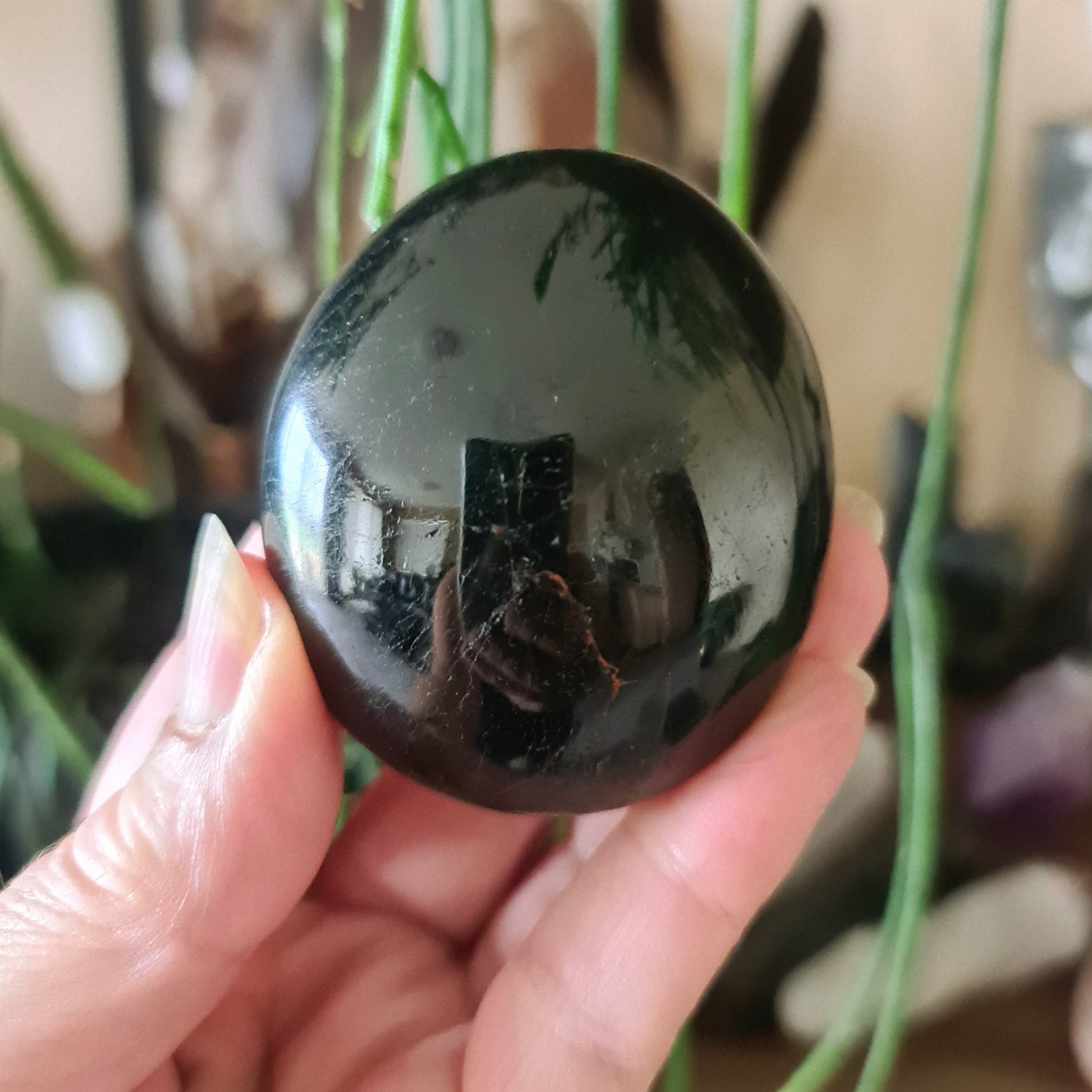 A hand holding a polished black obsidian palm stone, with a mirror-like surface.