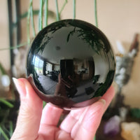 A hand holding a large black obsidian sphere with a reflective surface.