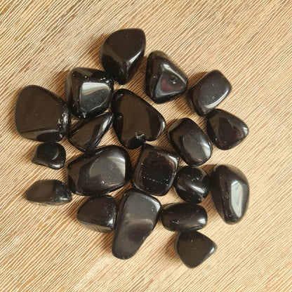 A collection of black obsidian stones on a wooden surface.