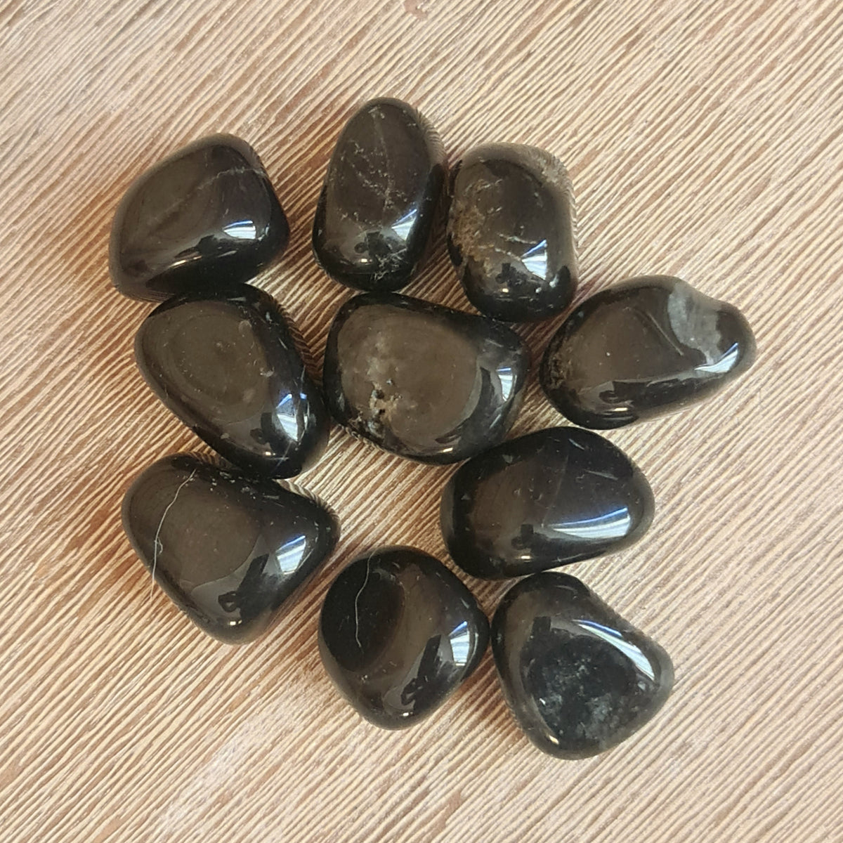 A collection of black onyx tumble stones arranged in a pattern on a wooden surface.