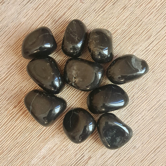 A collection of black onyx tumble stones arranged in a pattern on a wooden surface.