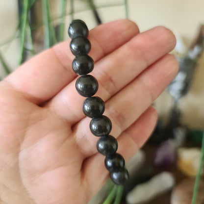 A hand holding a black tourmaline bracelet with a series of beads.