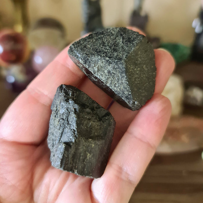 Two pieces of Black Tourmaline held in a person's hand, showing the rough, dark surfaces of the stones.