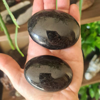 Two polished black tourmaline palm stones with natural white lines, held in a person's hand.