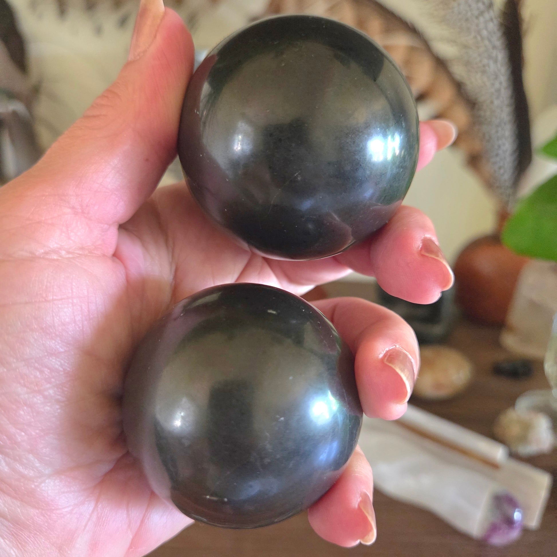 Two dark green crystal balls held in a hand with a blurred background