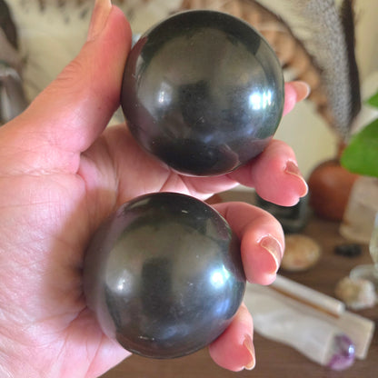 Two dark green crystal balls held in a hand with a blurred background