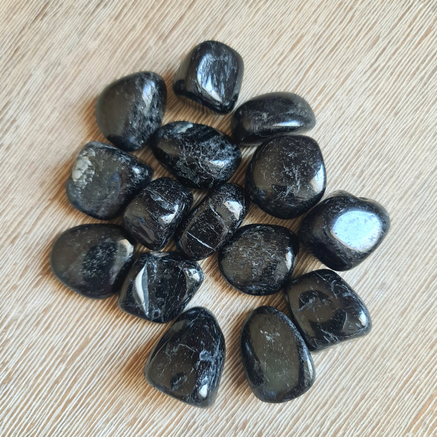 A collection of Black Tourmaline tumble stones displayed on a wooden surface.