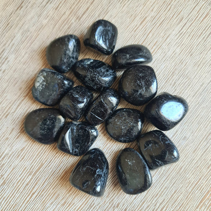 A collection of Black Tourmaline tumble stones displayed on a wooden surface.