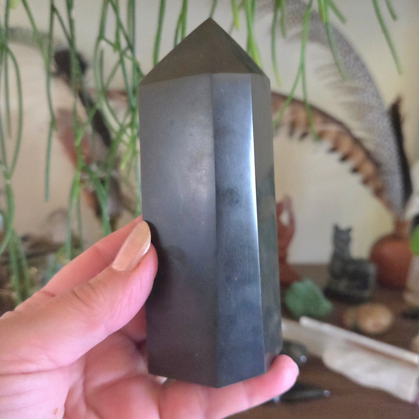 Hand holding a dark crystal pyramid with a blurred indoor background