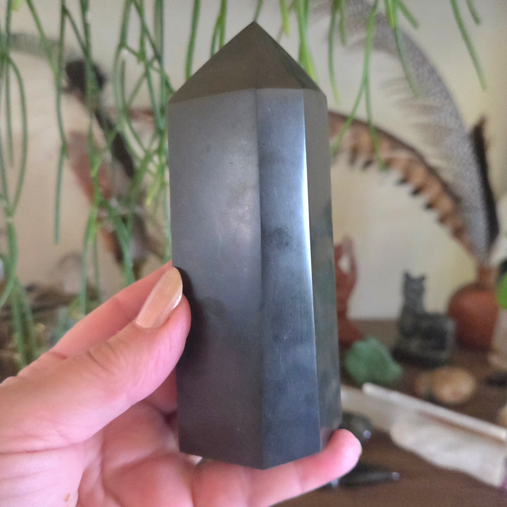 Hand holding a dark crystal pyramid with a blurred indoor background