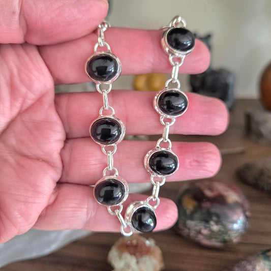 Silver bracelet with black beads held in a hand on a wooden surface.