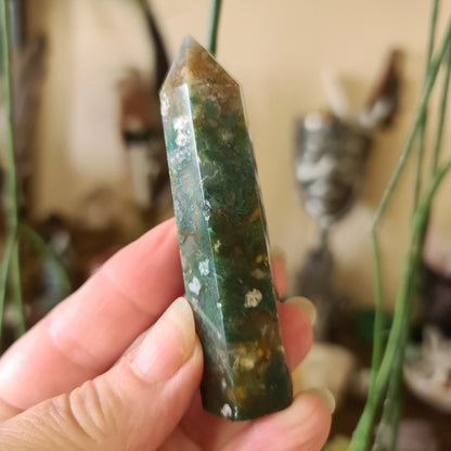 A hand holding a polished Bloodstone point with a greenish tint and natural pattern.