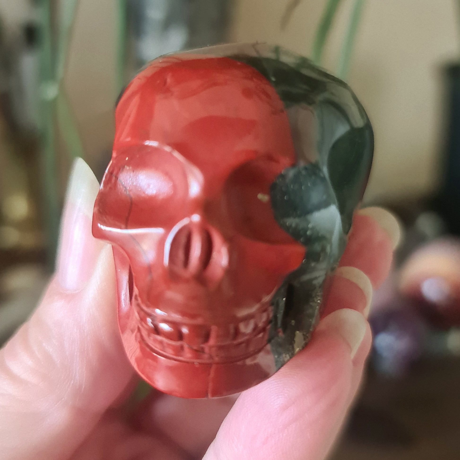 A hand holding a red and black crystal skull, with a person's fingers visible on the side.