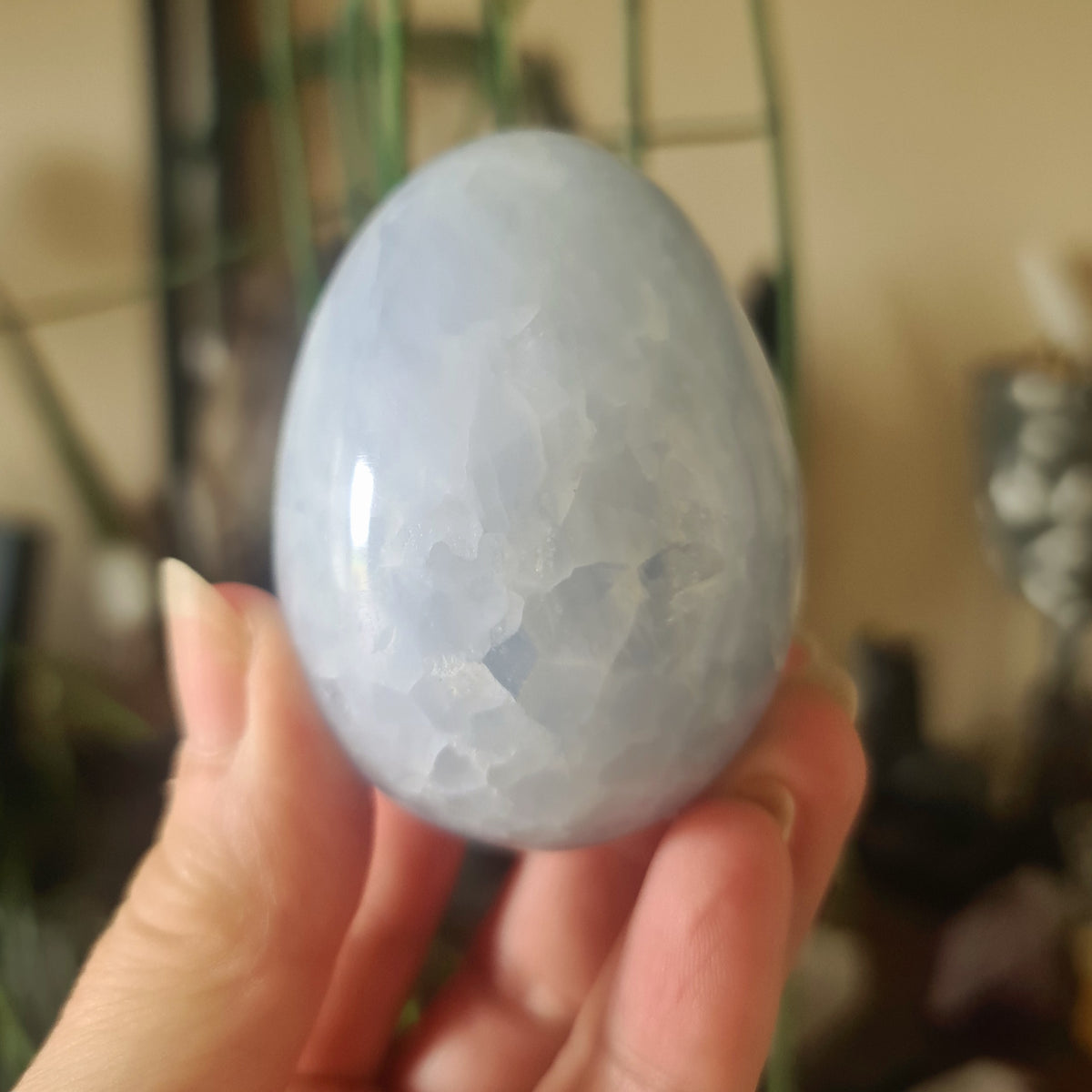 A hand holding a smooth blue calcite egg with a cracked surface.