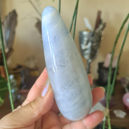 A hand holding a blue calcite massage stone with a smooth, polished surface.