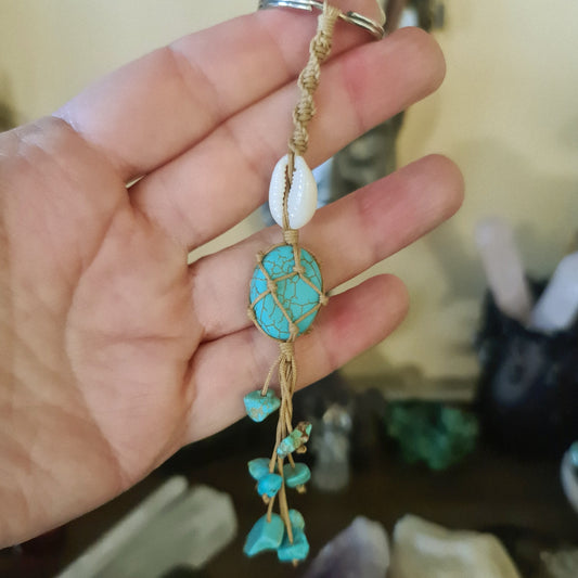 A hand holding a keyring with a blue howlite cowrie shell attached to a piece of macrame.