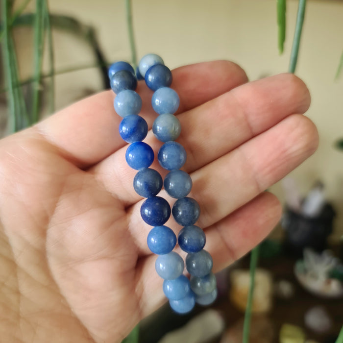 A hand holding a blue quartz bracelet with multiple stones.